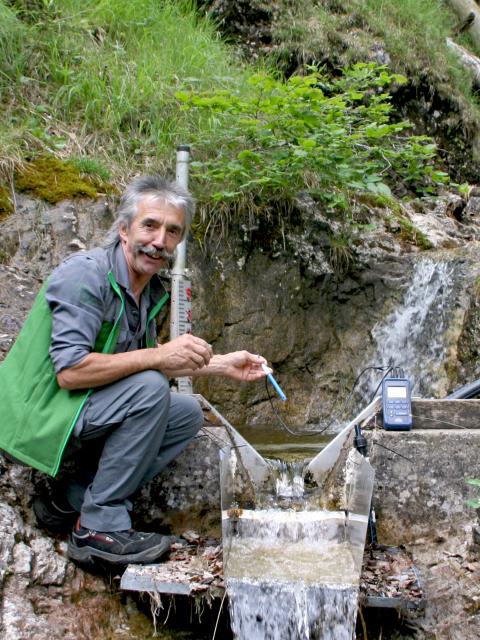 National Park employee measures water temperature of small mountain channel in steep terrain
