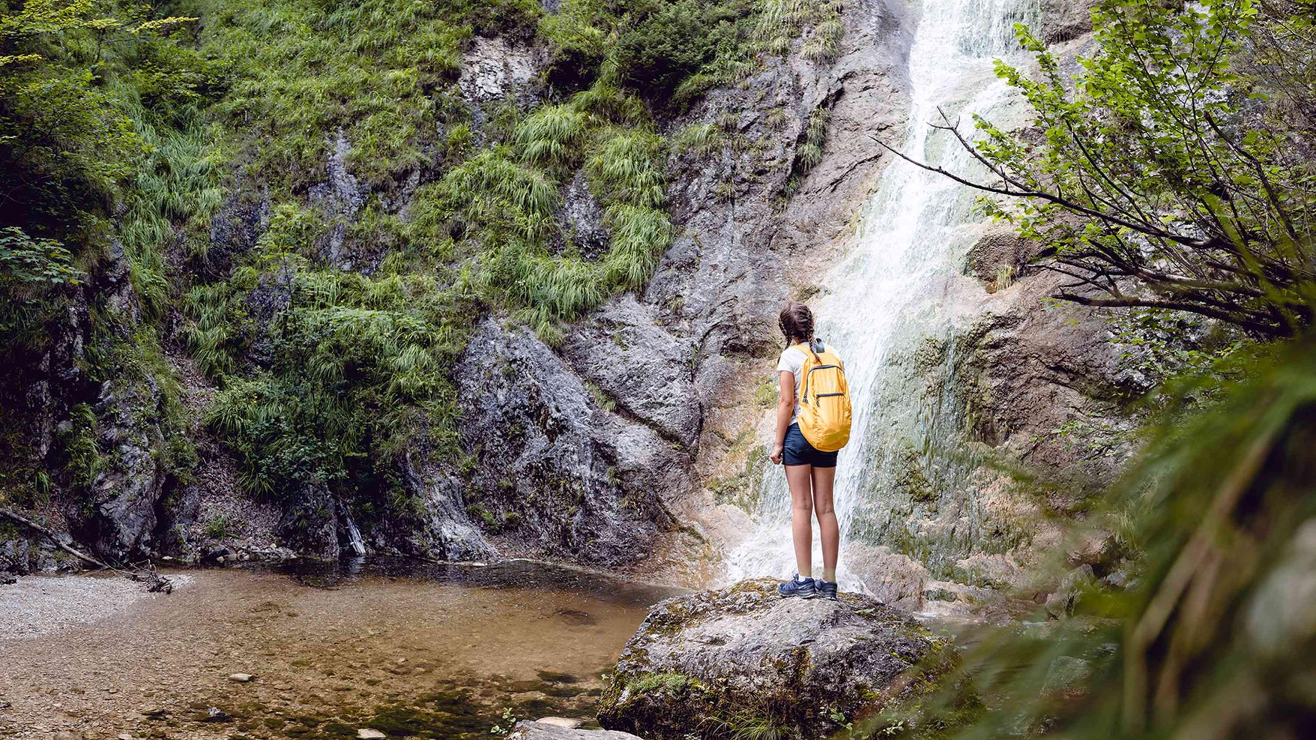 A woman stands on a rock in front of a waterfall