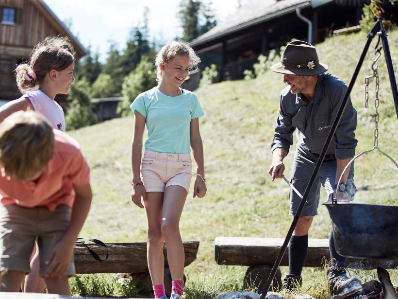 National Park Range and three children cook kettle soup together around the campfire