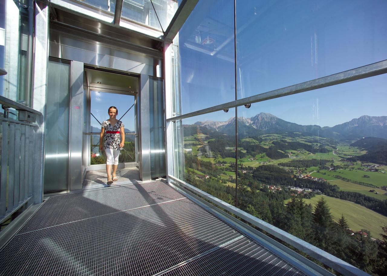 A young girl steps out of a glass elevator onto a viewing terrace