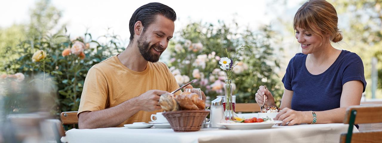 A couple dines at a laid table on a garden terrace