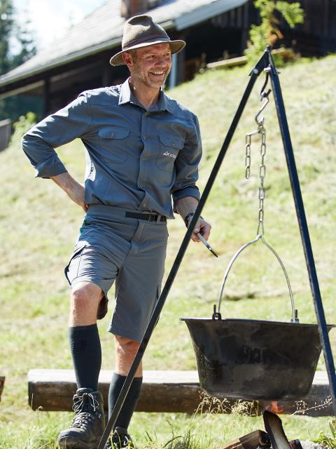 A national park ranger cooks in a cauldron hanging over a campfire