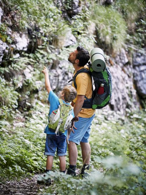 Father and son stand on a hiking trail and look up at a rock