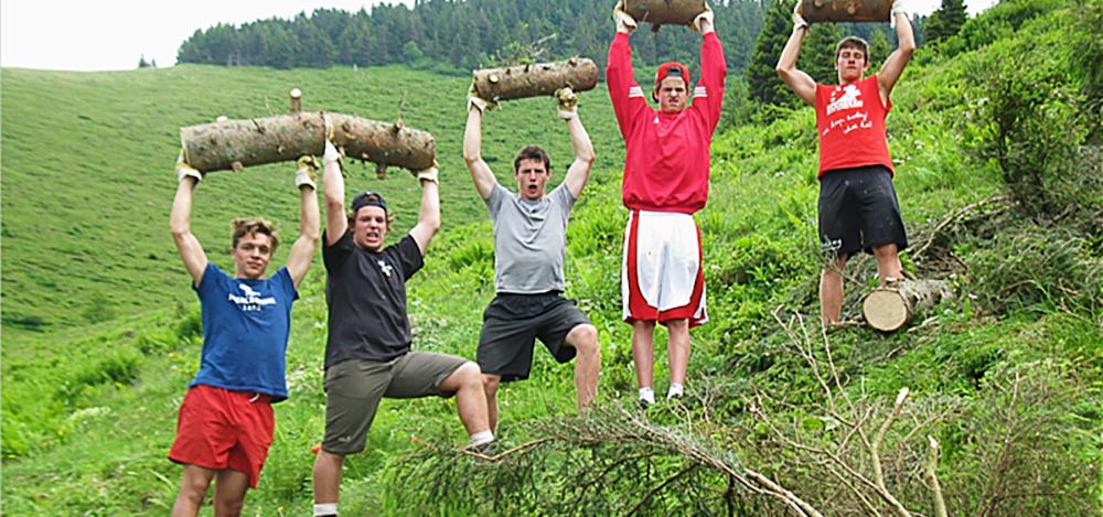 Five boys each triumphantly hold a piece of a spruce tree trunk above their heads