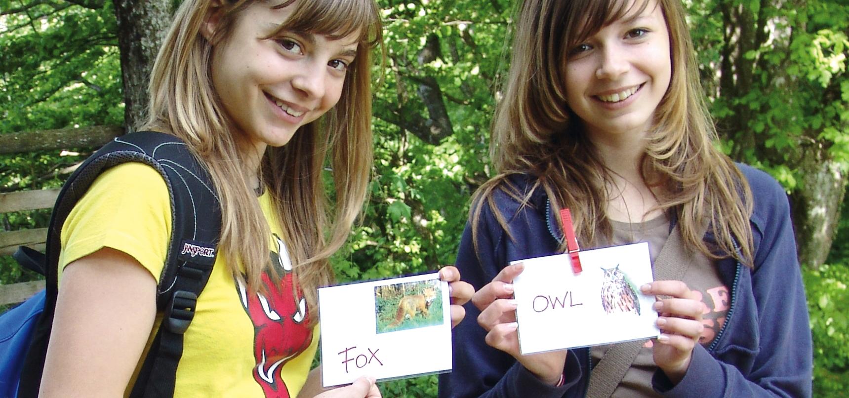 Two girls holding animal cards labeled in English