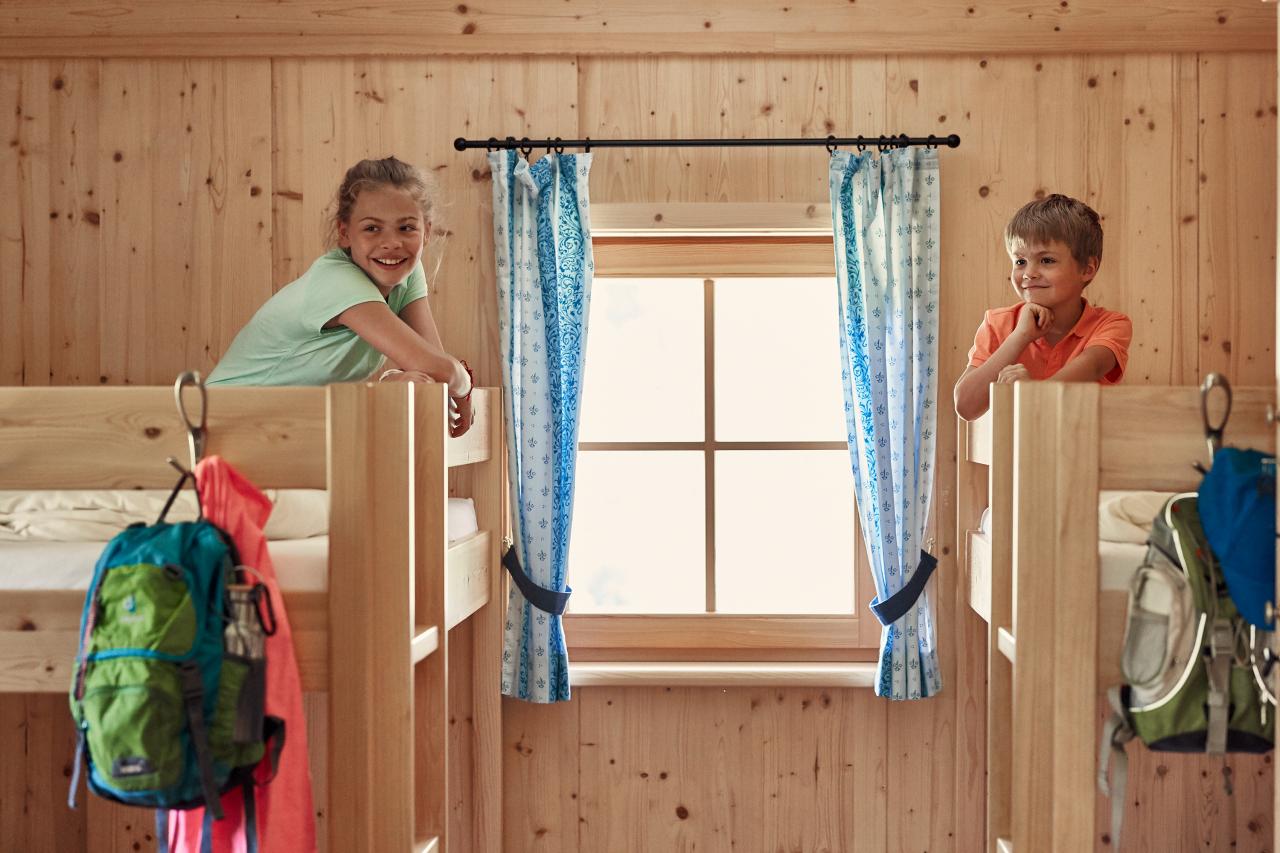 Two children sit in bunk beds in a wood-paneled room