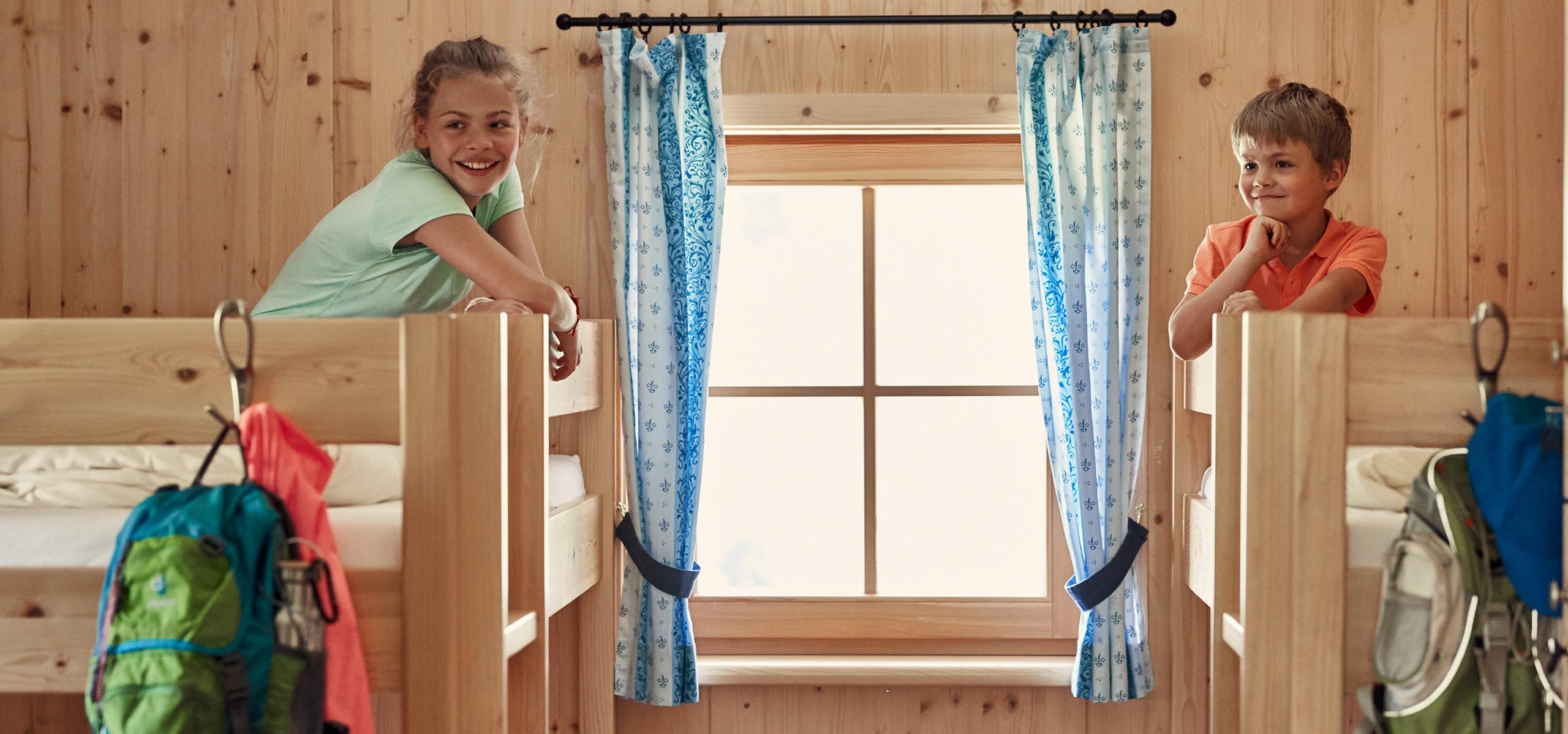 Two children sit in bunk beds in a wood-paneled room