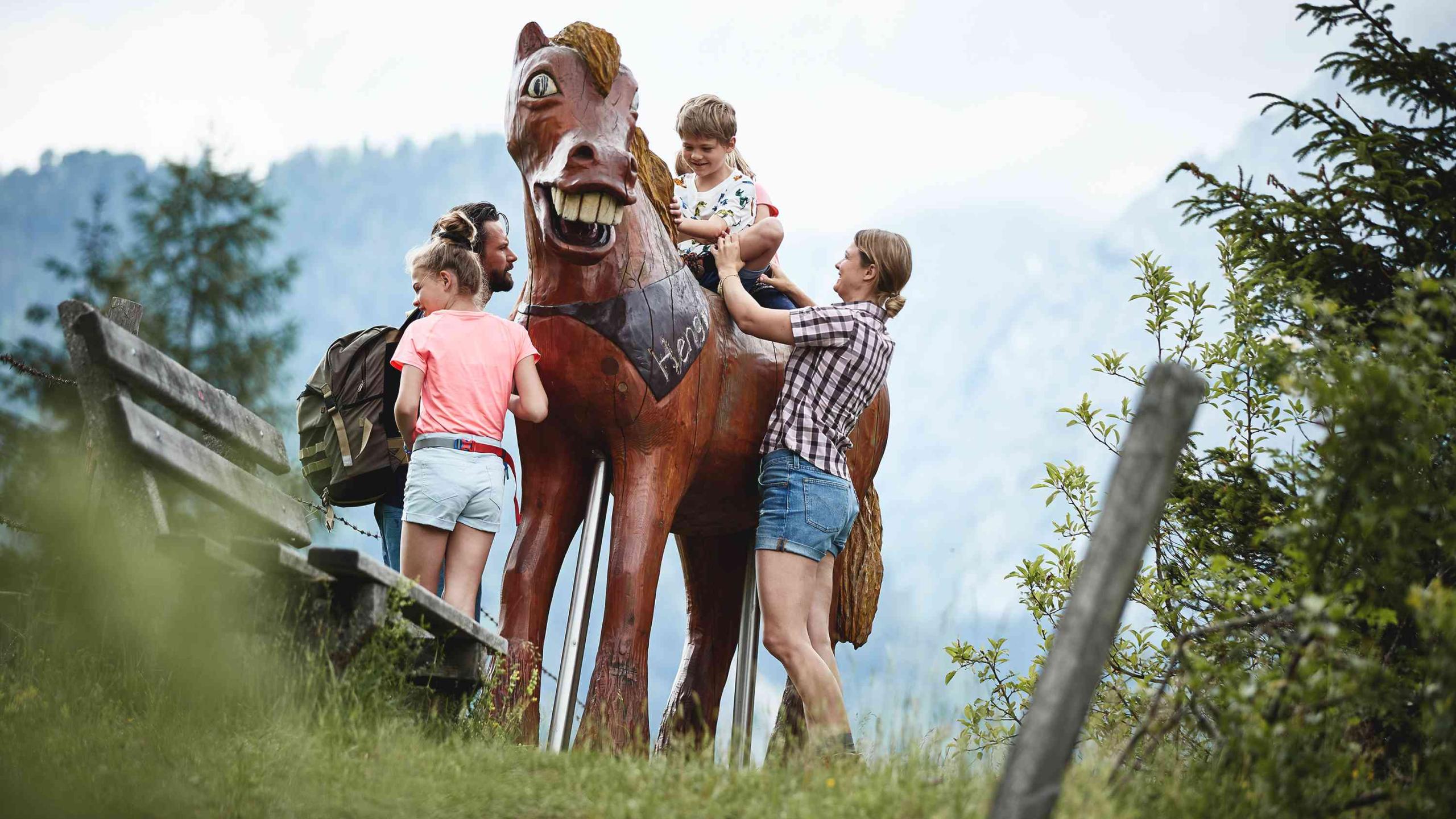 A child sits on a life-size wooden horse surrounded by his family