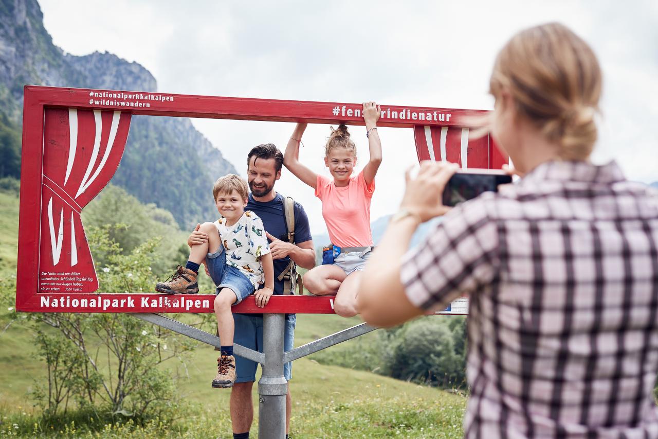 Woman taking a photo of a man and two children in a selfie photo frame on an alpine meadow