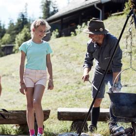 National Park Range and three children cook kettle soup together around the campfire