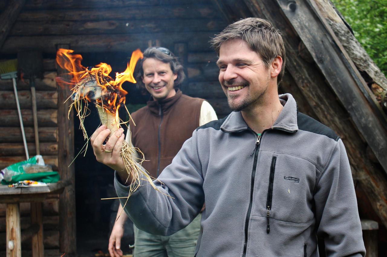 Two men light a fire in a piece of birch bark filled with grass