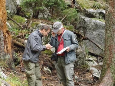 Two researchers stand in the forest and look at an insect sitting on a finger