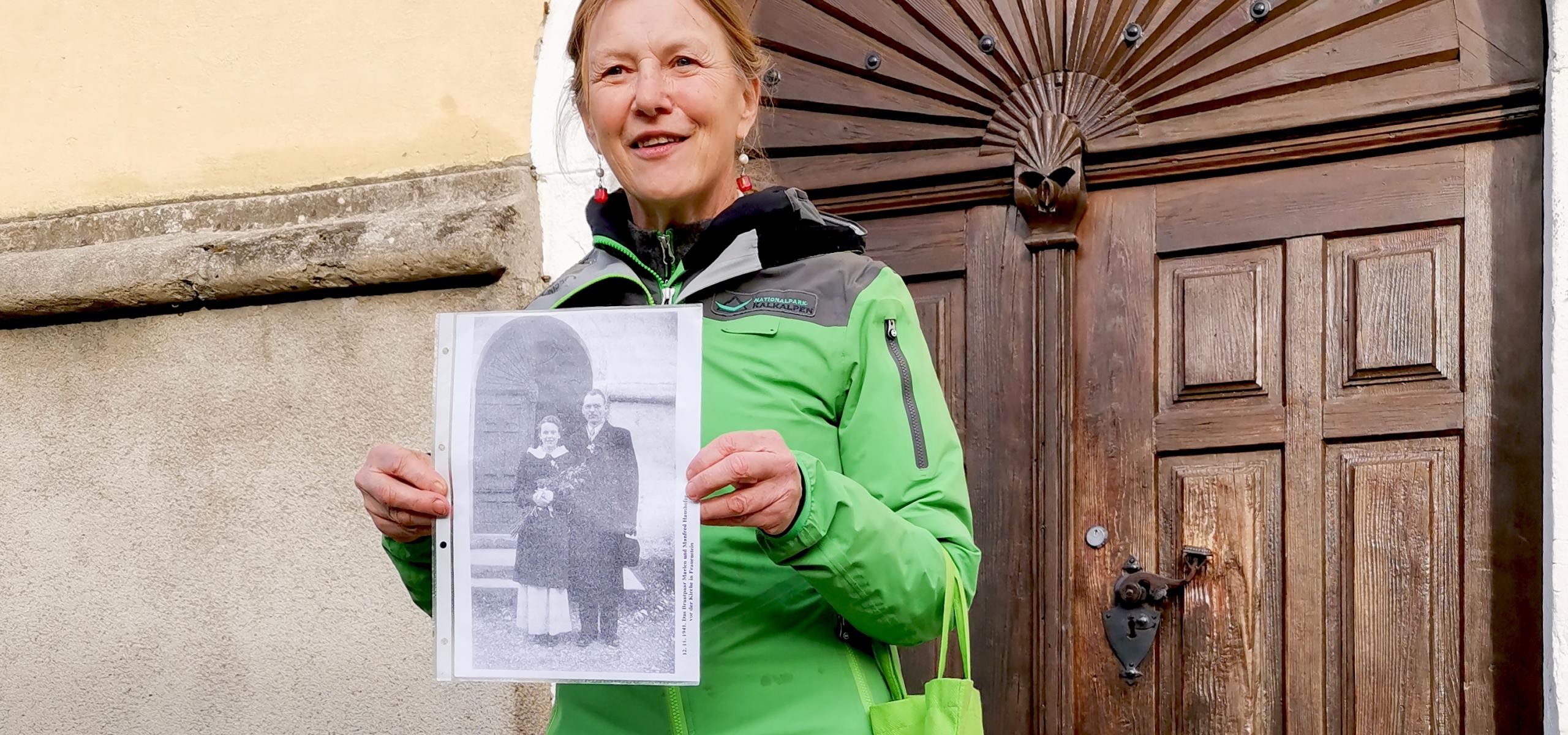 Ranger stands in front of the church portal showing the old wedding photo of Marlen Haushofer in her hand