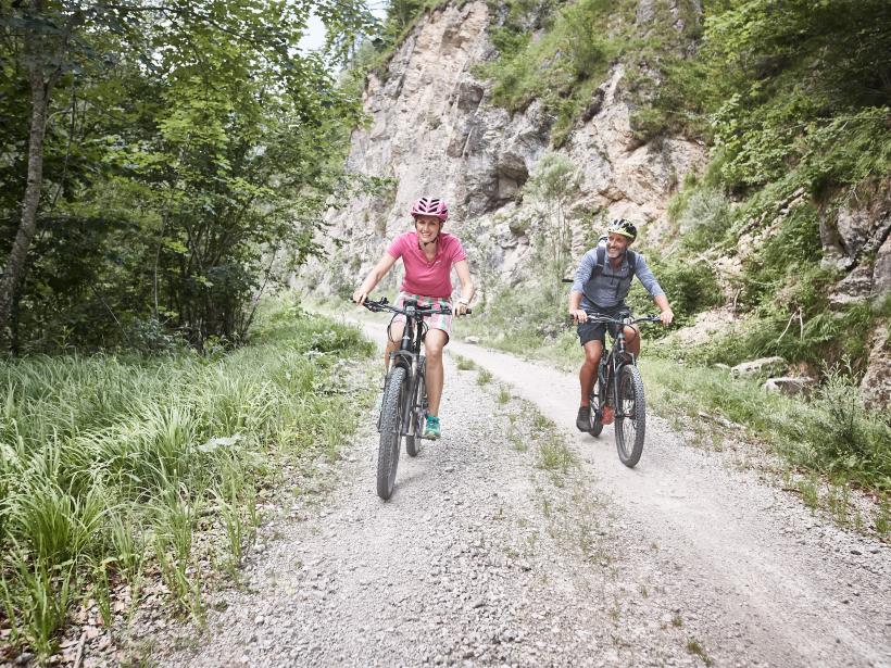 A woman and a man ride e-mountain bikes on a gravel road