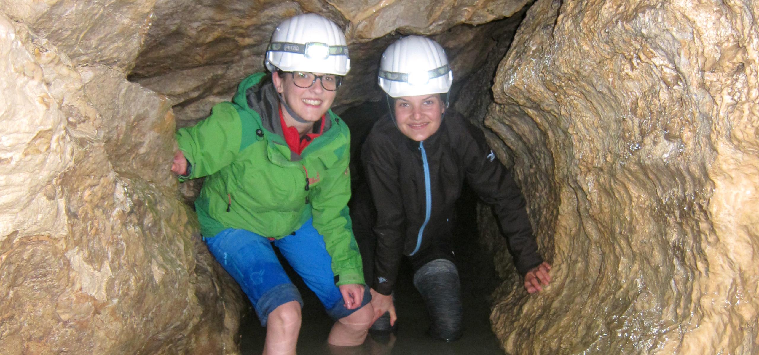 Two children wade knee-deep through the water in a cave passage