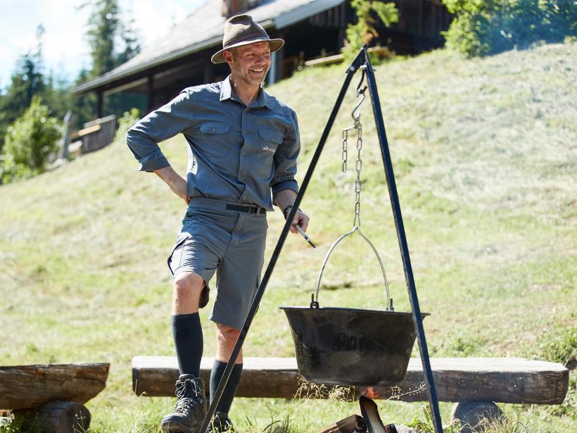 A national park ranger cooks in a cauldron hanging over a campfire