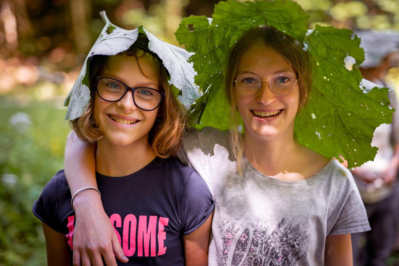 Two girls have put a large coltsfoot leaf on their heads