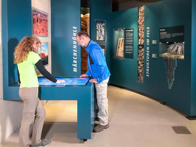 A woman and a man stand at a desk with a flatscreen in the Fascination of Rock exhibition