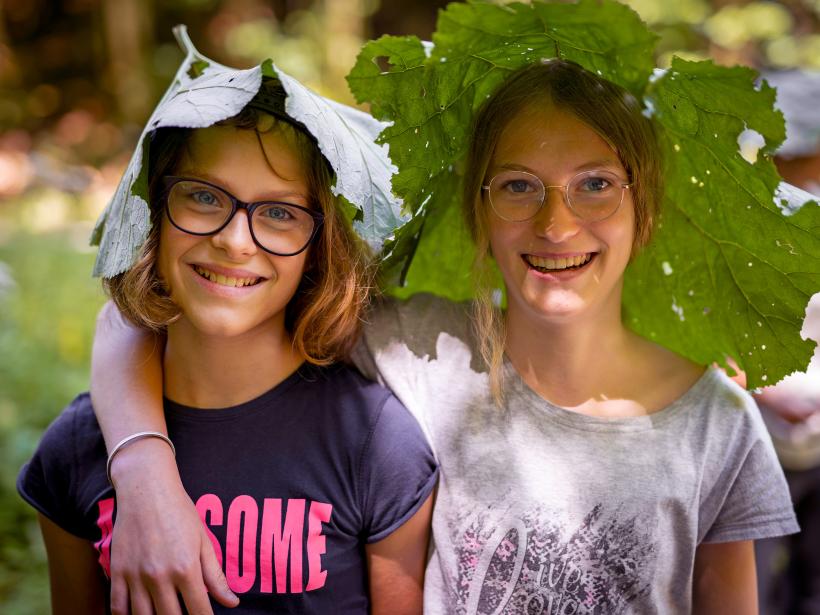 Two girls have put a large coltsfoot leaf on their heads