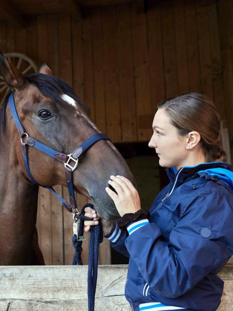 A young woman stands next to her horse in a riding stable