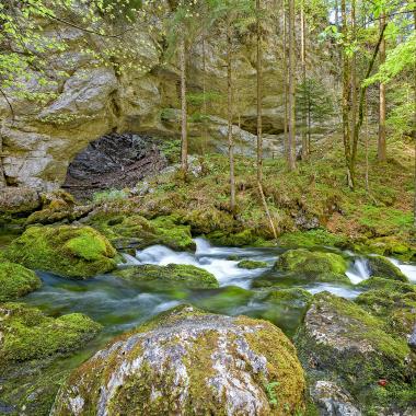 Spring runoff into a mossy mountain stream, behind it a rock arch - the so-called Devil's Church