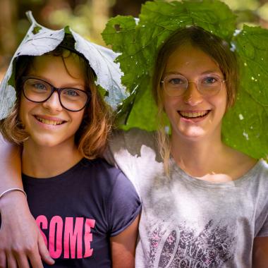 Two girls have put a large coltsfoot leaf on their heads