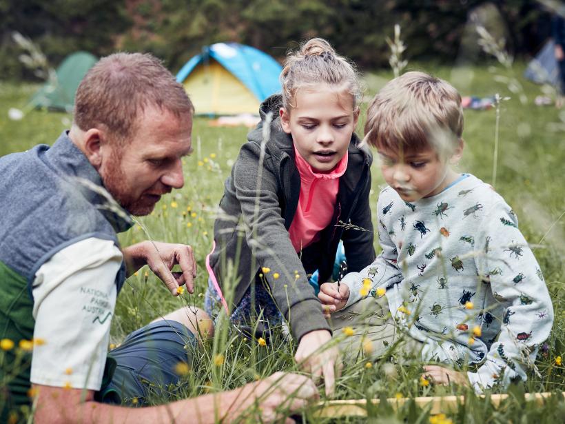 National Park Ranger and two children sit in the grass and learn about bird feathers