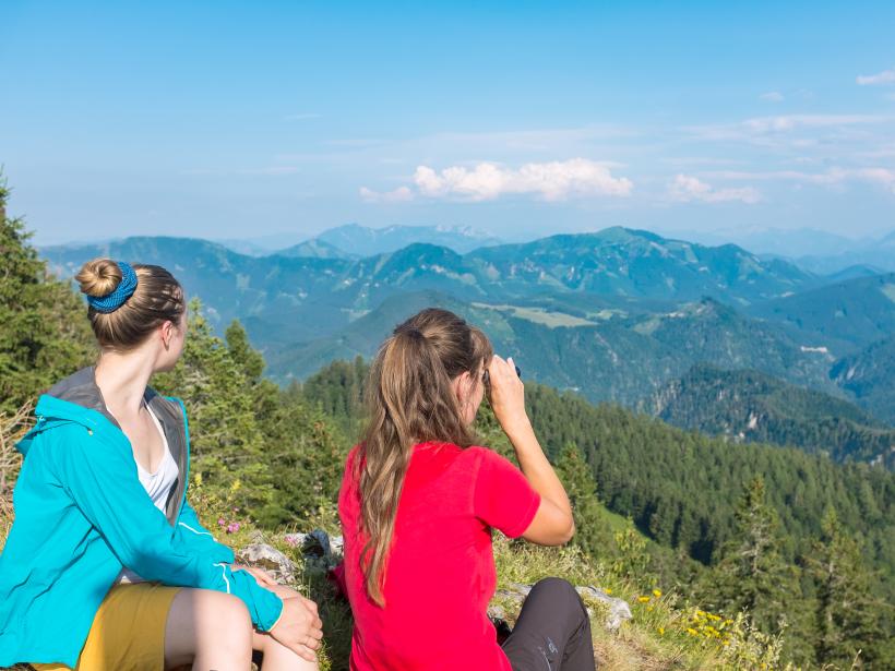 Two women sit on a mountain top and look over the mountain panorama