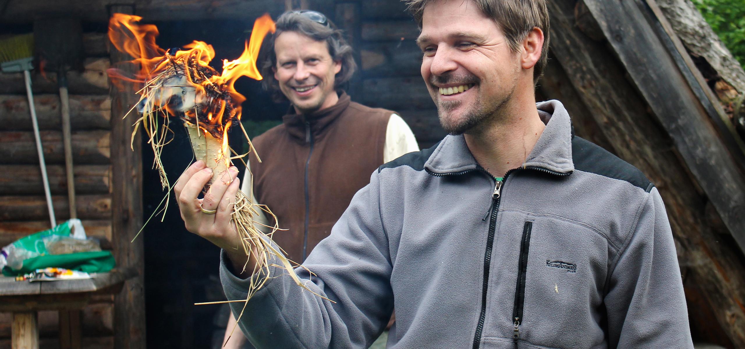 Two men light a fire in a piece of birch bark filled with grass