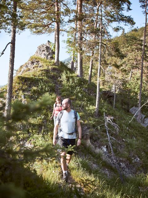 A woman and a man hike along a narrow path in a rocky forest