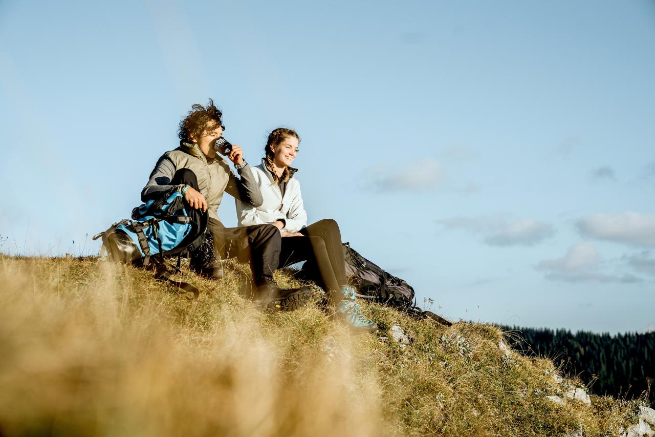 A woman and a man sit on a mountain ridge in the sun and rest