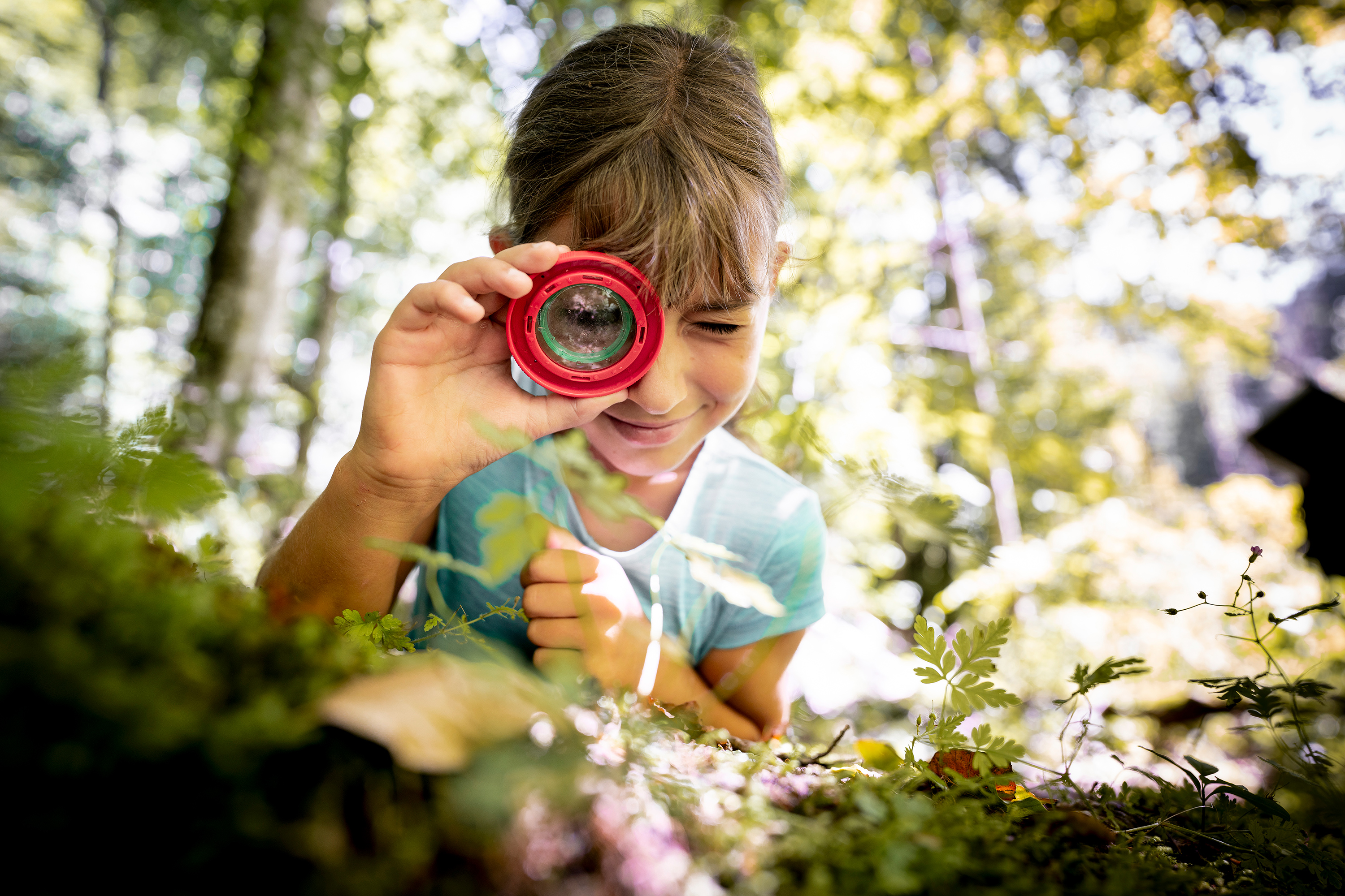 A girl observes the forest floor through a magnifying glass